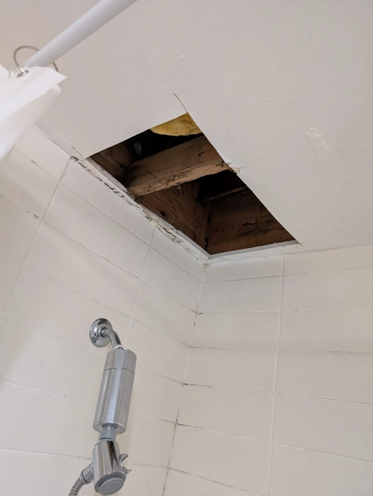 Water-damaged bathroom ceiling cut open above the shower, exposing joists and insulation