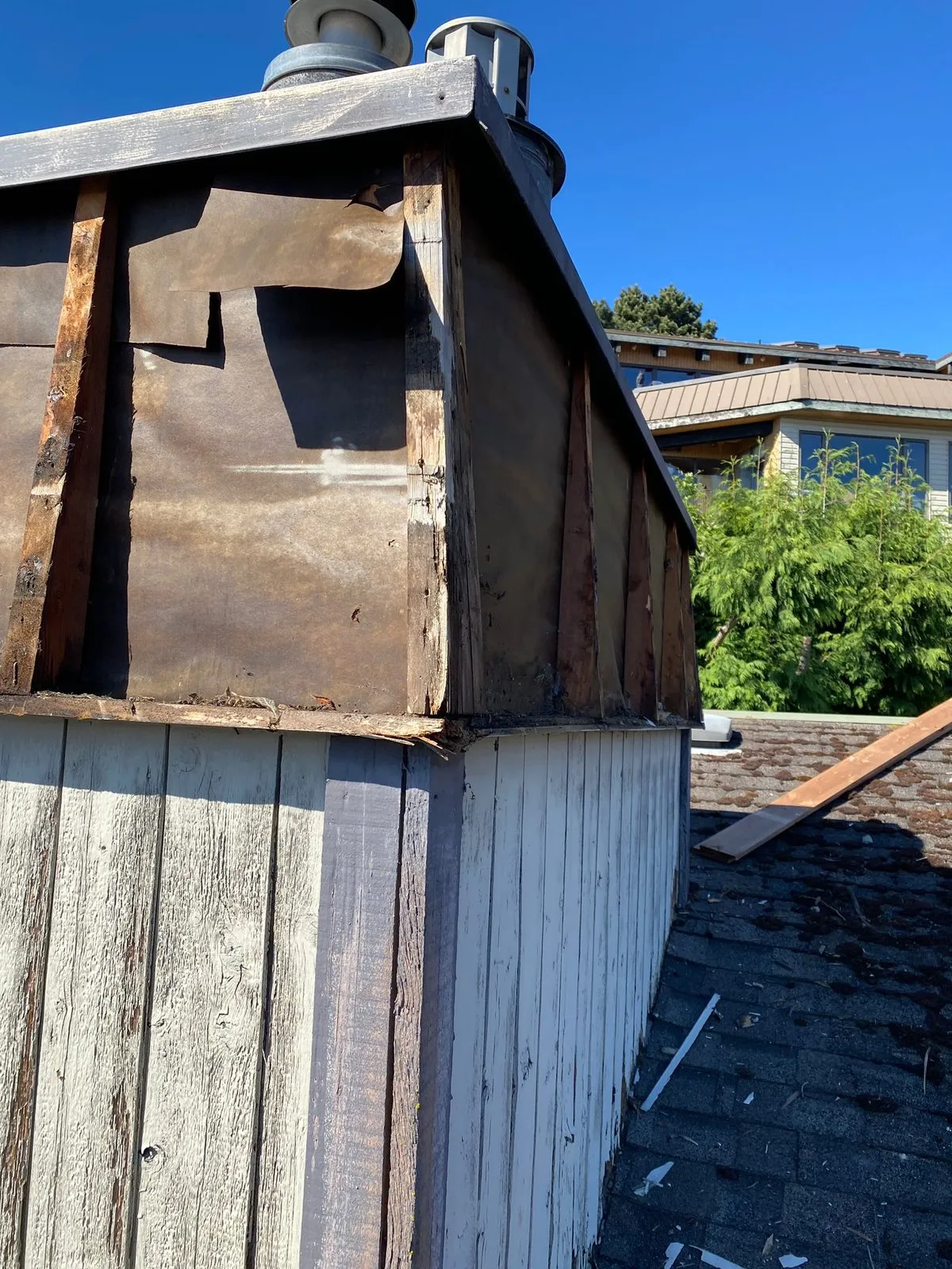 Rooftop chimney chase with siding stripped off, exposing rotted framing and old building paper